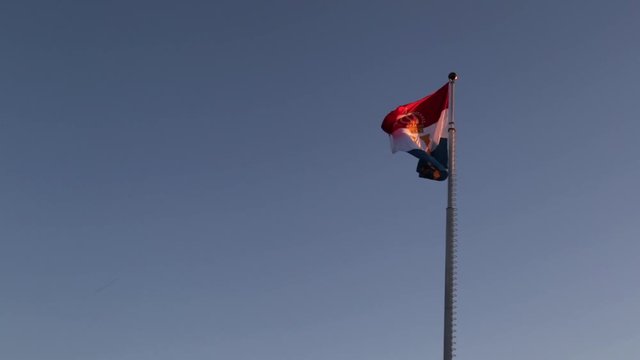 Flag of Luxembourg with royal monogram of Grand Duke Henri flying against a blue sky at sunset, in anticipation of Luxembourg's national holiday