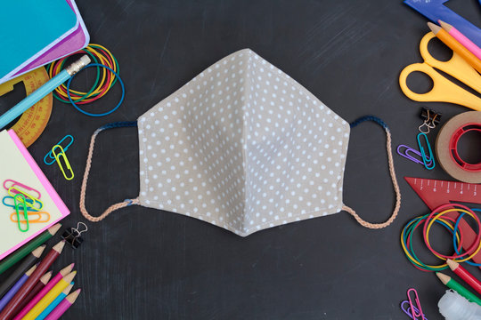Top view of School supplies and cloth mask on chalkboard. Back to school guidelines during covid-19 pandemic - Powered by Adobe