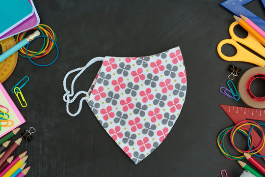 Top view of School supplies and cloth face mask on chalkboard. Back to school guidelines during covid-19 pandemic