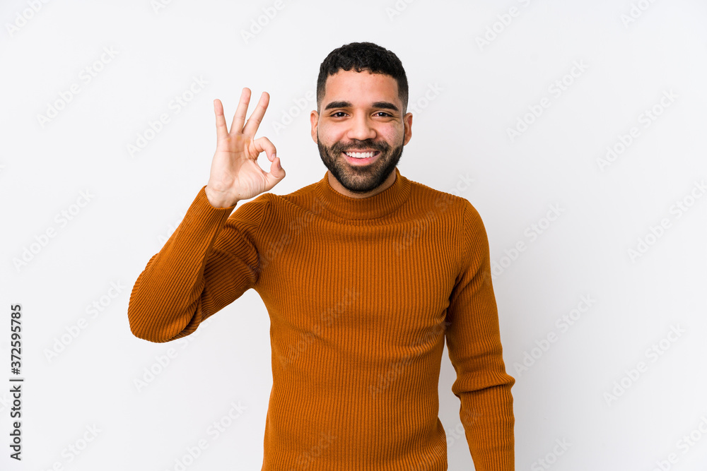 Wall mural young latin man against a white background isolated cheerful and confident showing ok gesture.