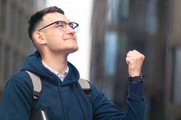 Happy positive successful college student, cheerful pupil, young handsome man with book smiling in glasses, looking at result list. Smart boy passed university exam, test, celebrating victory, triumph