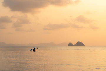 Naklejka na ściany i meble Couple kayaking on the sea against the backdrop of islands and golden sunset