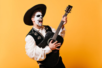 Guy singing emotional song plays guitar. Portrait of man with painted face in sombrero