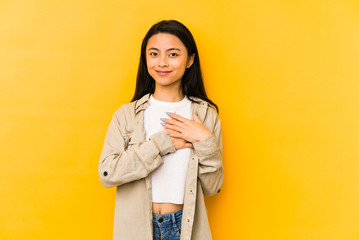 Young chinese woman isolated on a yellow background has friendly expression, pressing palm to chest. Love concept.