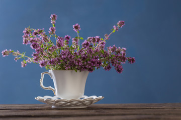 thyme flowers in white vintage cup on wooden table on blue background