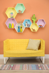 Sofa near orange wall with hexagon shaped shelves in room. Interior design