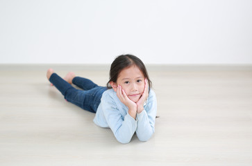 Portrait asian little child girl lying on wood laminate flooring in the room with looking at camera.