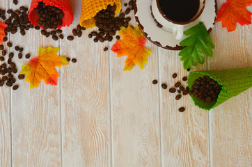 Autumn background with copy space for text and design. A cup of coffee, coffee beans waffle cones and autumn leaves. Cozy atmosphere and warm mood