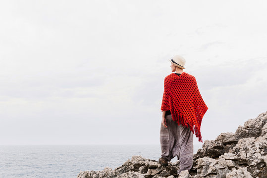 Full length back view of woman in stylish clothes standing on edge of rocky cliff against cloudy sky and admiring seascape while enjoying holidays on Asturian coast of Spain