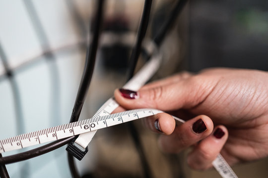 Cropped unrecognizable seamstress taking measurements of wire dummy standing in loft style studio