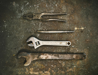 Top view set of various metal instruments for metalworking including wrenches and pliers arranged on grunge gray surface