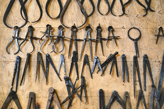 Set of various metal jewelry instruments on wooden wall representing pliers and bench pins on wooden weathered wall in studio