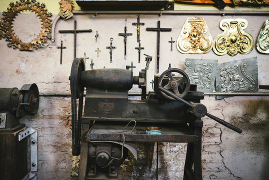 Aged metal rolling mill machine with steering wheel near shabby wall with collection of crosses and ornamental golden items in studio