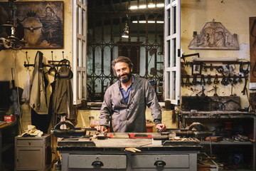 Front view of happy craftsman cleaning etching with creative ornament in golden frame using hard piece of fabric in workshop