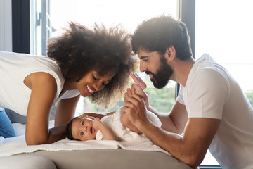 Side view of delighted multiethnic family playing with cute baby on sofa at home