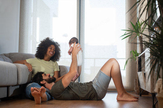Content multiracial mother and father playing with adorable baby while resting on floor in modern apartment
