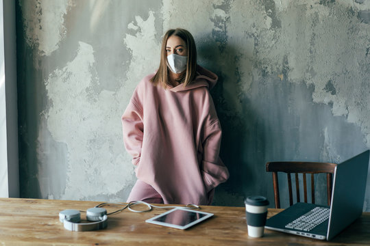 Unrecognizable discontent female in pullover and sterile mask standing with crossed arms near cement wall with shabby surface in flat and looking at camera during COVID 19 pandemic
