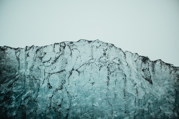 Textured surface of frozen ice with particles of black volcanic sand against cloudy sky on Diamond beach of Jokulsarlon lagoon in Iceland