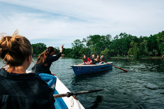 Group of young friends floating on boats along peaceful river while chatting and gesticulating with raised arm in Saint George, Transylvania, Romania