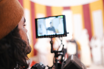 Back view crop male video operator in hat broadcasting live event and looking at display on camera