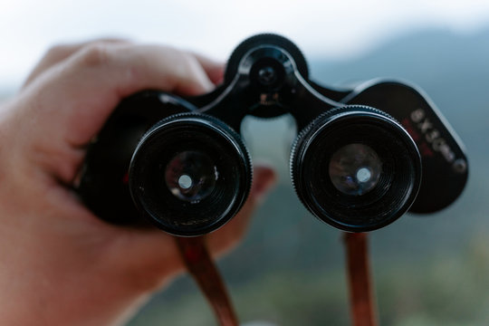 Crop anonymous hiker holding binoculars while observing nature in mountainous terrain in summer day