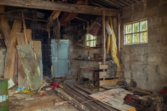 Interior of abandoned fisherman house with metal door and brick wall with outfit and different wooden boards with shabby surface in daylight