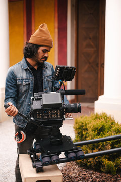 Side view faceless male video operator in casual denim jacket and hat shooting video of actor on modern professional camera