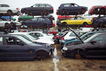 Rubbish dump with pile of multicolored modern automobiles after accident with dents on surface on wet road under blue sky in town