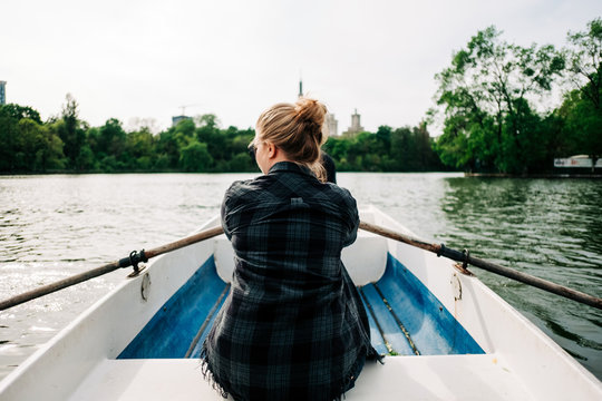 Back View Of Unrecognizable Woman In Casual Outfits Sculling Boat With Oars On Calm Peaceful Lake In Summer