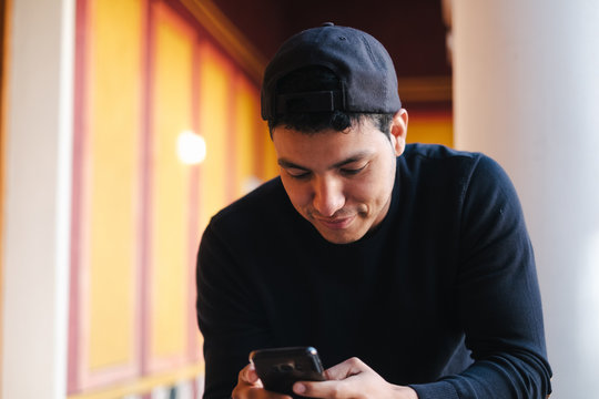Cheerful male in black casual wear and hat surfing modern mobile phone while spending time in contemporary creative studio