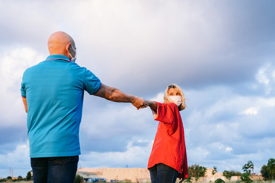 Romantic Middle Age Couple In Respirators And Casual Clothes Holding Hands And Spinning While Walking Together In Countryside During Summer Evening And Looking At Each Other With Love