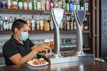 Ethnic woman pouring beer into glass from beer column while working as barkeeper in modern bar