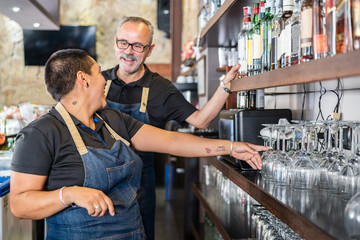 Side view of male and female bar coworkers making drinks while talking to each other during working day