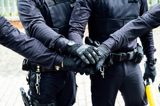anonymous police officers in protective gears and medical masks armed with guns and batons putting hands together while preparing for operation