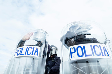 Low angle of anonymous police soldiers in protective uniforms and helmets standing against squad van and defending by riot shields