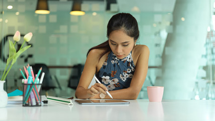 female fashion designer working with digital tablet on worktable in glass partition office