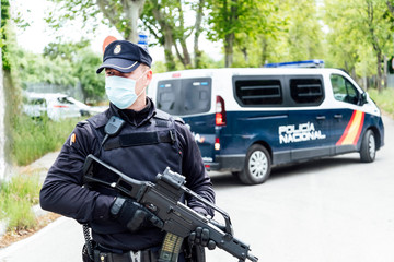 Concentrated police officer in uniform and medical mask looking away while patrolling street with automatic rifle