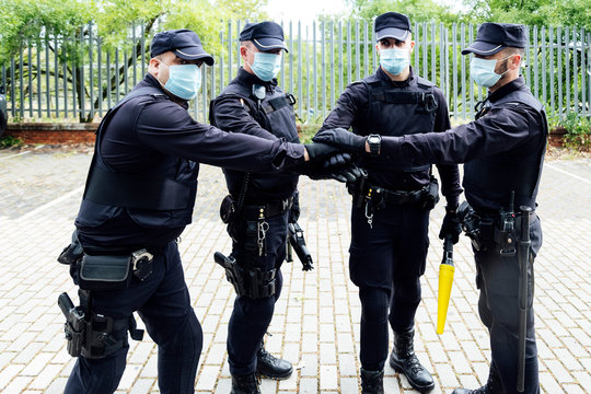 Serious anonymous police officers in protective gears and medical masks armed with guns and batons putting hands together while preparing for operation
