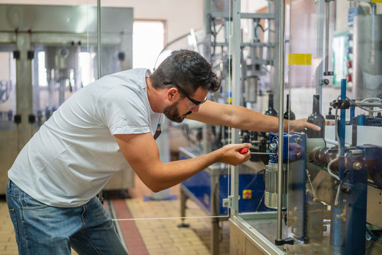 Side view concentrated bearded male winemaker in casual wear working with professional winery equipment in factory