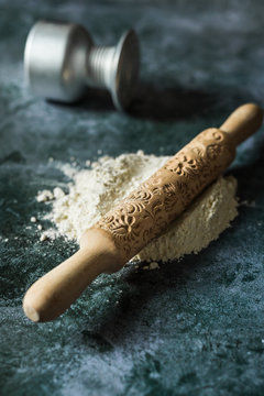 From above of composition of white flower with wooden rolling pin with floral decoration on surface near fallen bowl on dark stone table