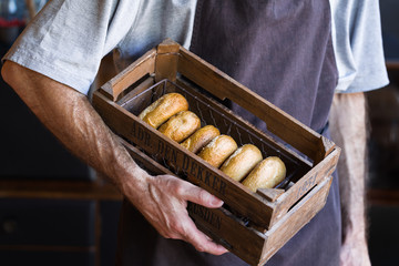 From above of crop unrecognizable male baker in apron standing with wooden box full of tasty freshly baked doughnuts with golden surface and tender texture