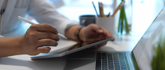Close up view of male hand using digital tablet and holding coffee cup on worktable