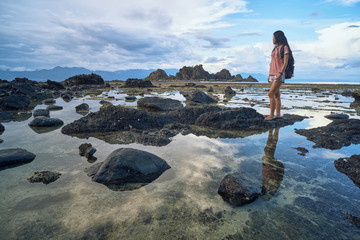 Full body of young woman with backpack enjoying view on sea and stony seaside during summer trip in Baler