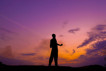 The silhouette of a man standing on a cliff with cool light in the sky.