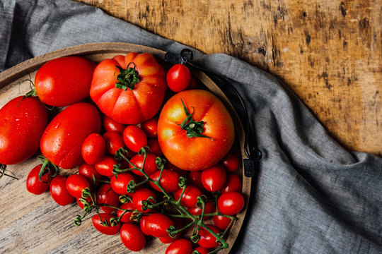 Top view of various types of fresh ripe red tomatoes on wooden tray arranged on rustic wooden table with cloth - Powered by Adobe