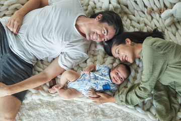 Parents lying down with their soon on a carpet, they are enjoying the time together at home