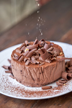 Closeup of palatable chocolate cheesecake sprinkled with cocoa powder and decorated with chocolate shavings served on white plate
