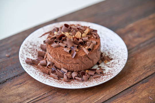 Closeup of palatable chocolate cheesecake sprinkled with cocoa powder and decorated with chocolate shavings served on white plate