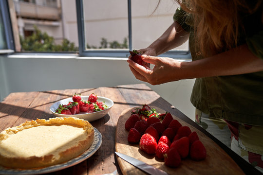 Female cook cutting fresh strawberry while preparing ingredients for homemade cake in kitchen