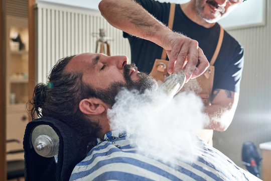 Crop barber treating beard of male client with talcum powder to relieve irritation and dry skin